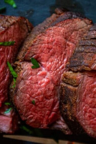 Slices of medium-rare beef tenderloin rest on a dark surface, garnished with parsley and ready for the best sauces.