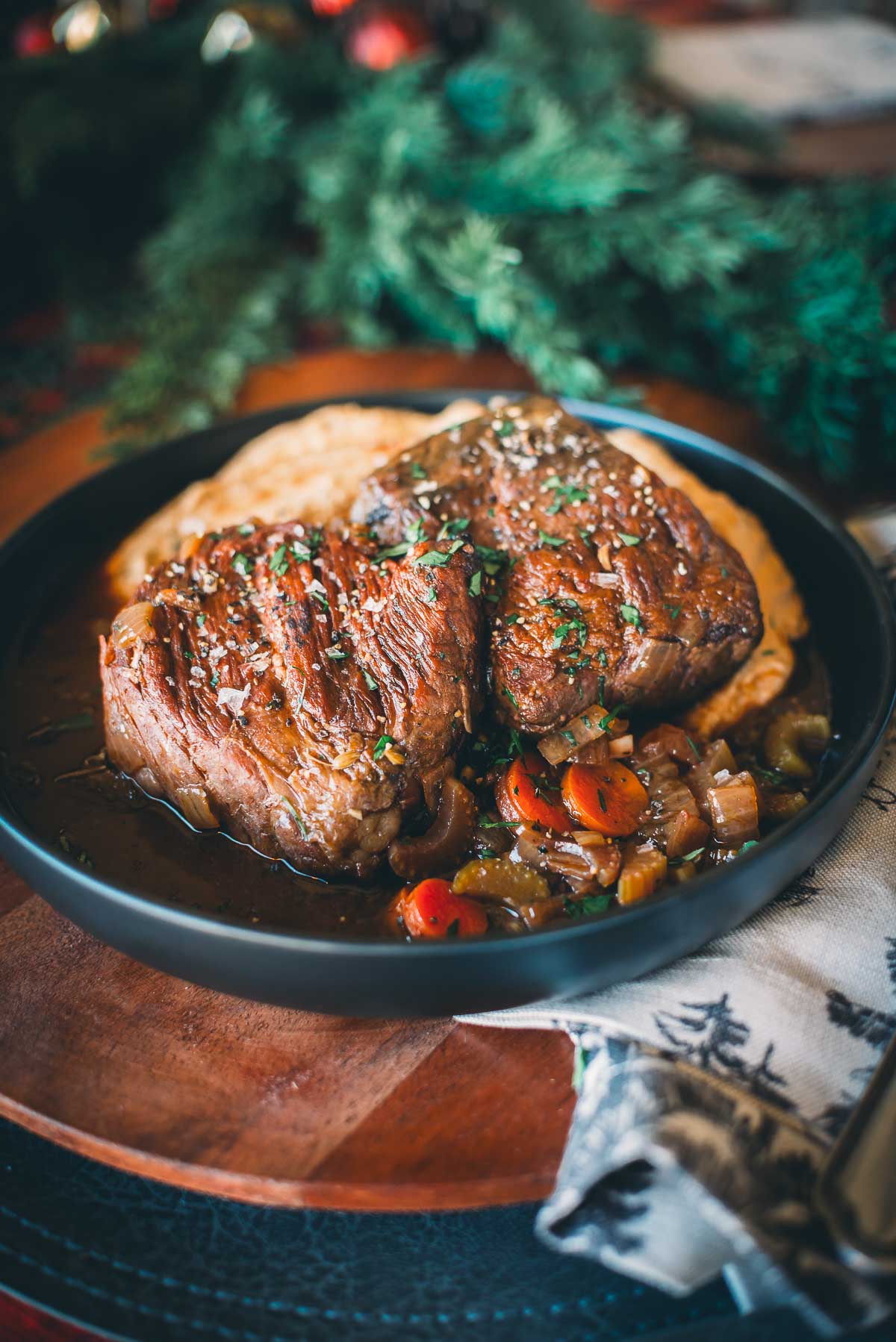 A plate of 48 hour sous vide short beef with herbs, served on mashed potatoes and garnished with chopped vegetables.