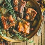 A plate of cider-braised pork short ribs with herbs on a wooden table. Text at the top reads "How to Make Cider Braised Pork Short Ribs.