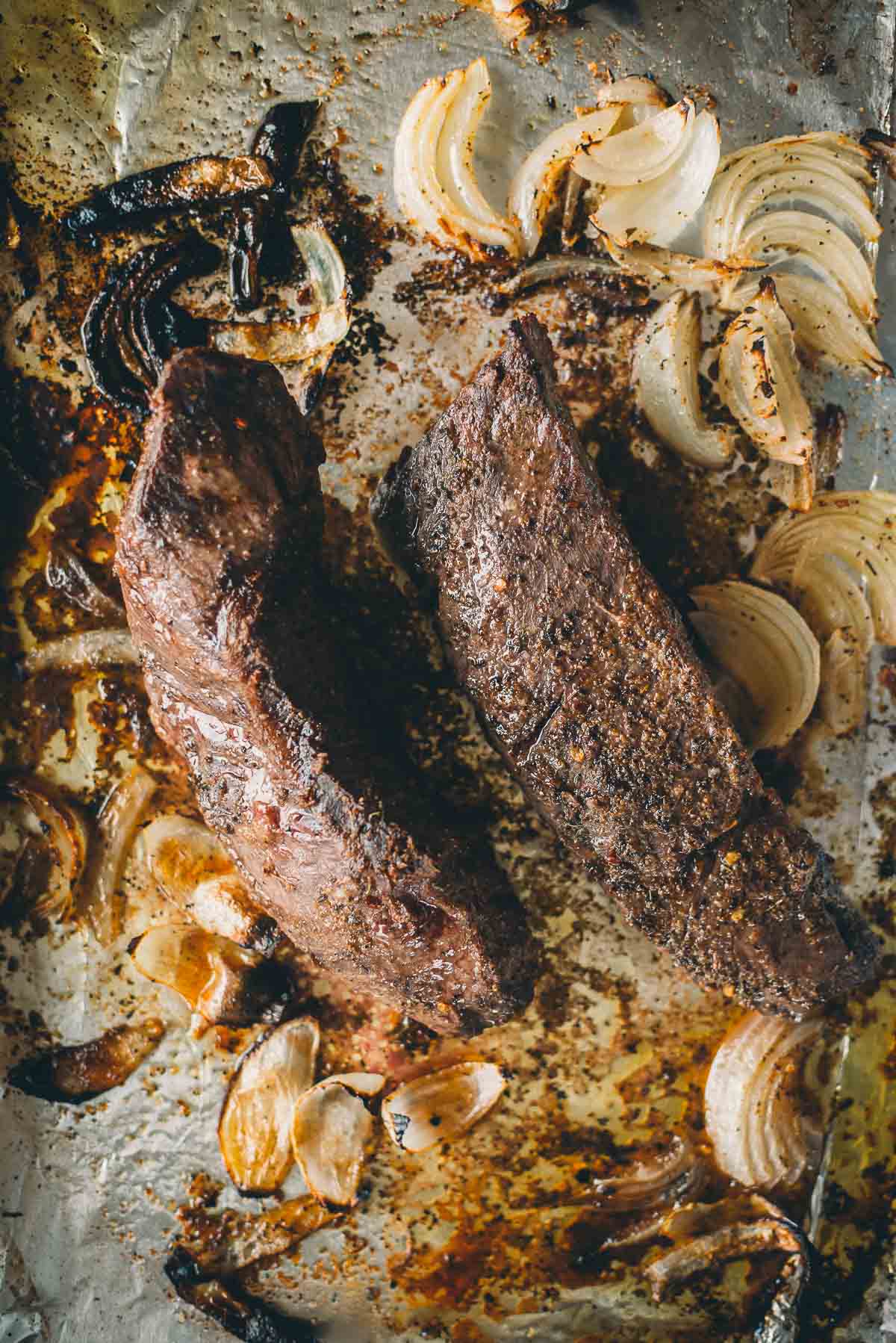 Two broiled hanger steaks on a baking sheet with roasted onion slices.