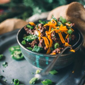 A bowl of venison chili topped with sliced green onions and shredded cheese, garnished with jalapeño slices.