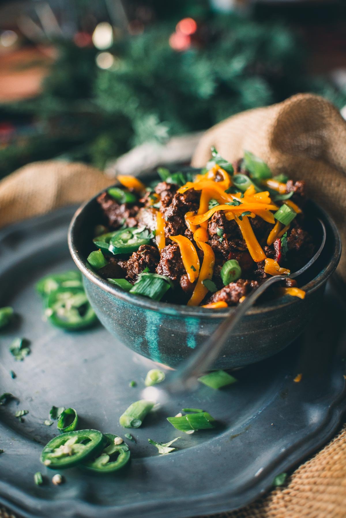 A bowl of venison chili topped with sliced ​​green onions and shredded cheese, garnished with jalapeño slices.