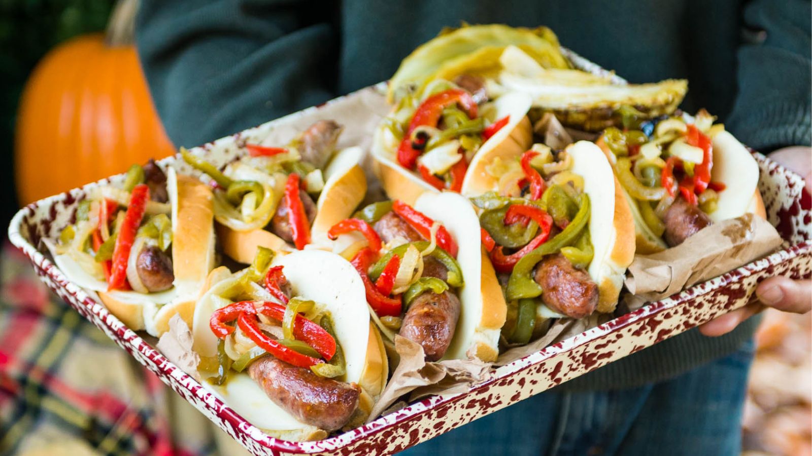 A tray of sausages in buns topped with grilled peppers and onions.