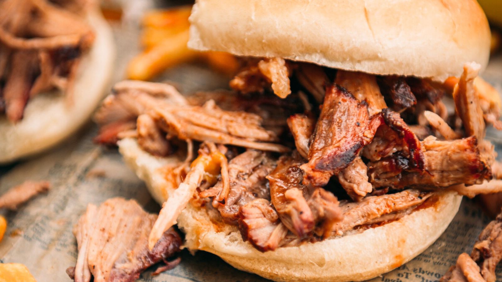 Pulled pork sandwich with tender meat in a bun on a piece of newspaper.