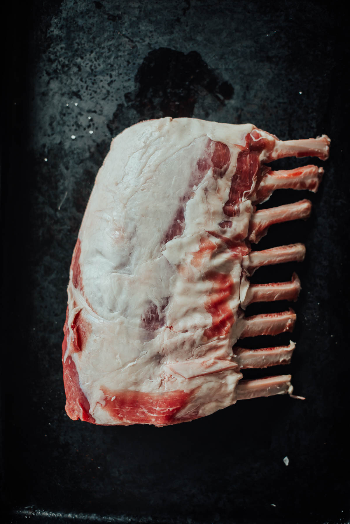 Raw rack of boar with visible bones on a dark, textured surface.