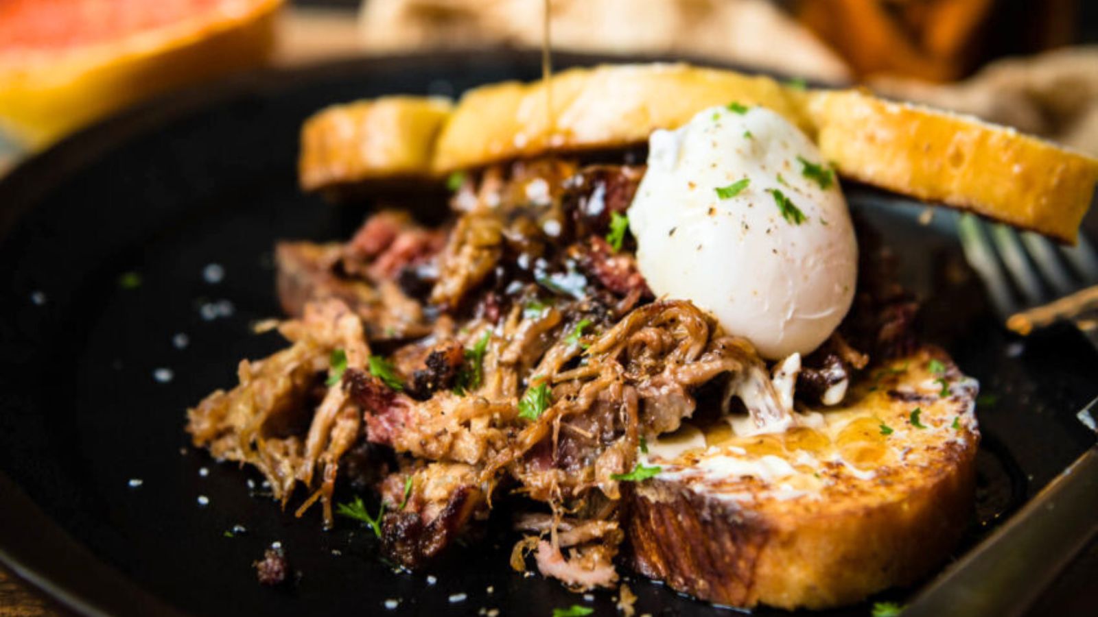 A poached egg rests on shredded beef atop toasted bread, garnished with herbs.