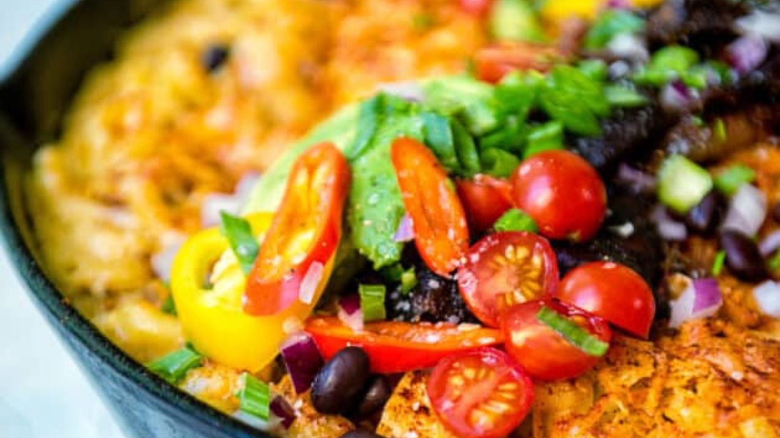 A colorful dish with cherry tomatoes, avocado, black beans, red onion, bell peppers, and a base layer visible in a black skillet.