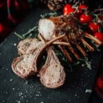 Sliced boar rack on a black slate platter, garnished with fresh arugula and cherry tomatoes, sprinkled with salt.