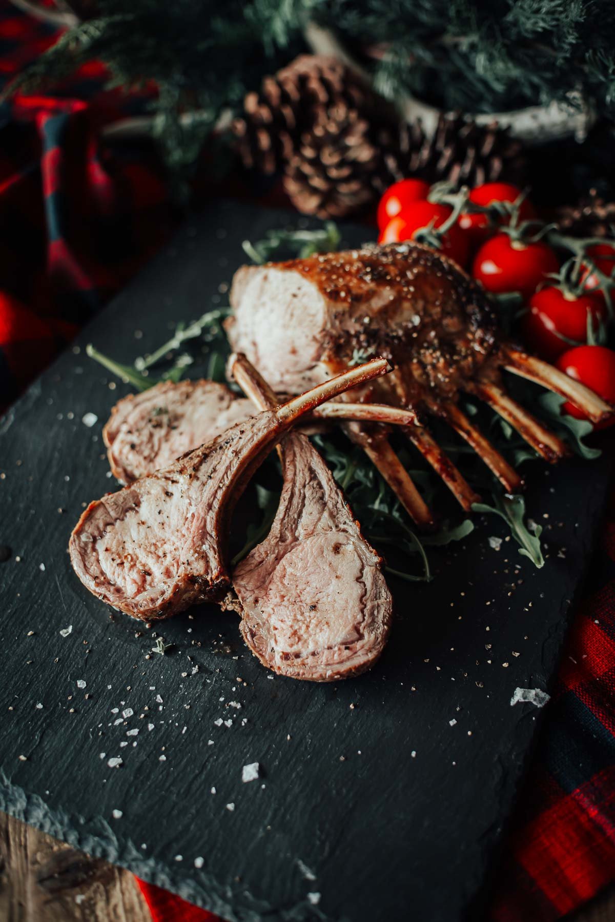 Sliced boar rack on a black slate platter, garnished with fresh arugula and cherry tomatoes, sprinkled with salt.