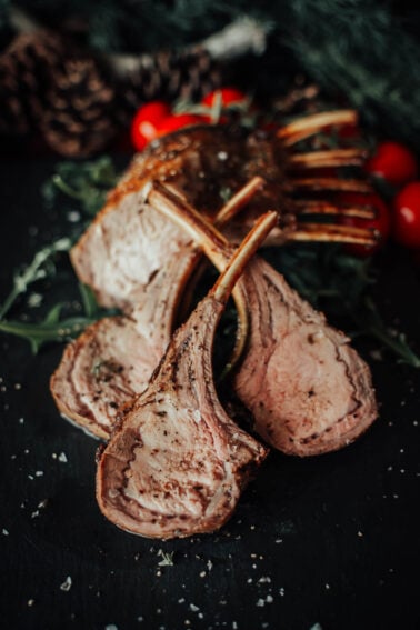 Slices of seasoned and cooked boar chops on a dark surface with cherry tomatoes and greens in the background.