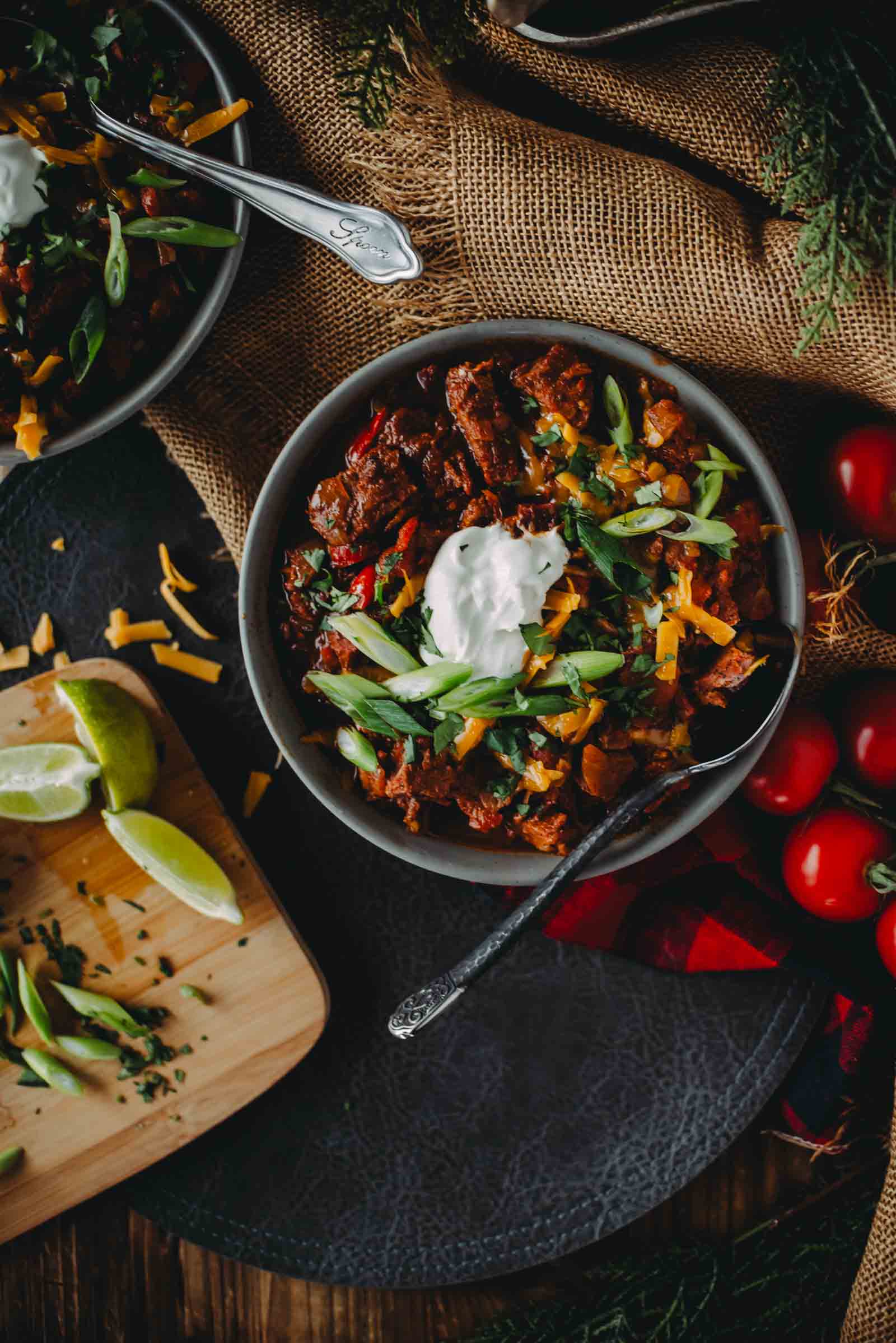 A bowl of brisket chili topped with sour cream and green onions, placed on a burlap cloth.