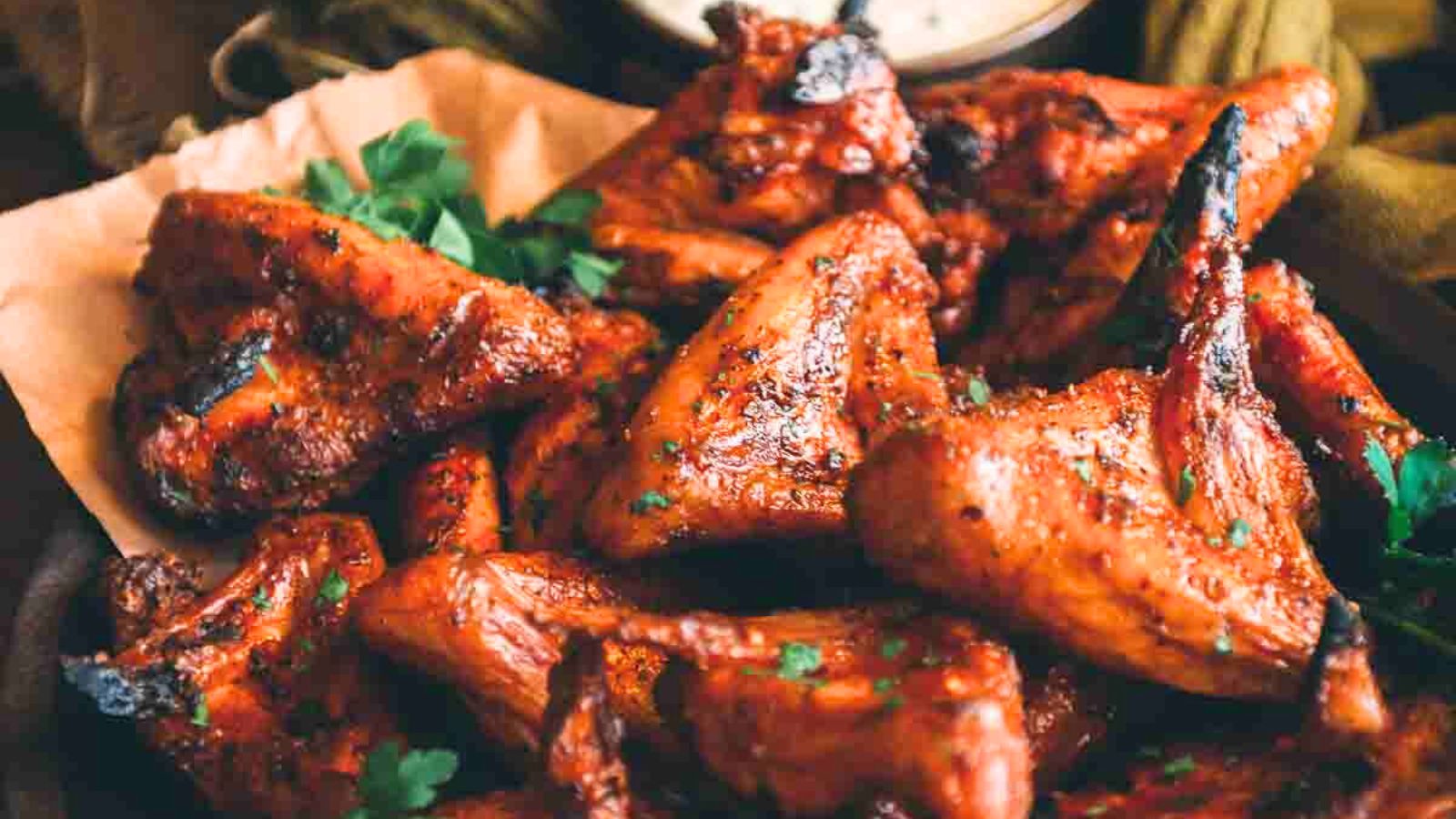 Close-up of spicy grilled chicken wings on parchment paper, garnished with parsley.