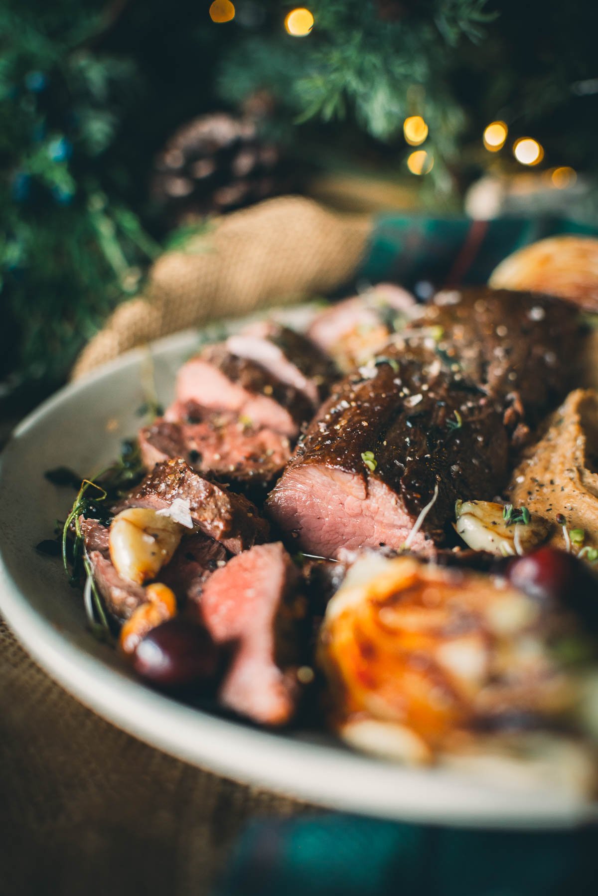 A plate of sliced sous vide venison tenderloin garnished with herbs, accompanied by roasted potatoes and vegetables.