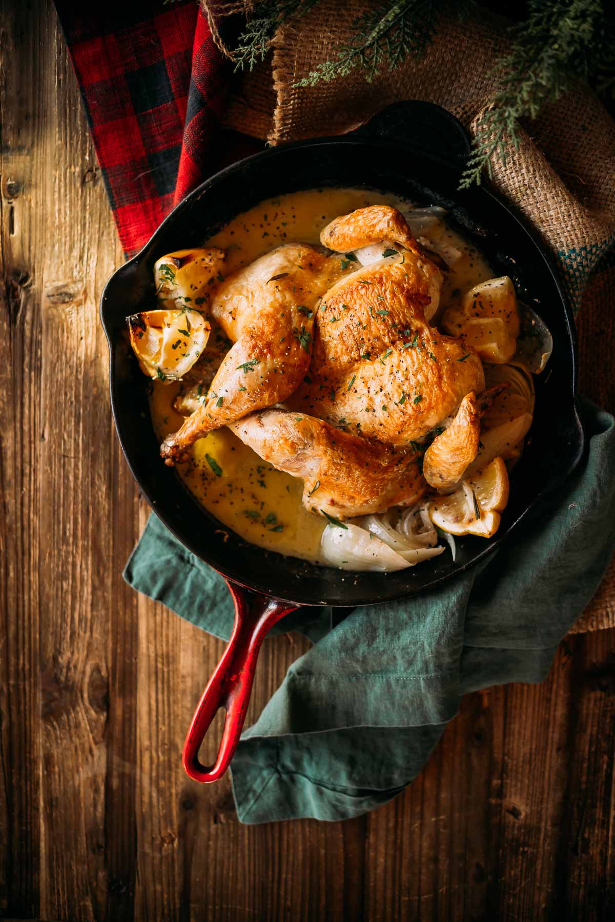 Chicken in cast iron skillet with lemon garlic sauce and herbs on a wooden table, featuring a rustic setting with a cloth napkin.