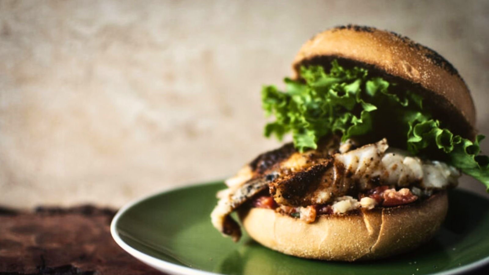 A grilled fish sandwich with leafy lettuce on a green plate against a textured background.