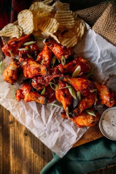 A platter of honey sriracha wings garnished with sliced green onions, served with crinkle-cut chips and a small bowl of dipping sauce on the side.