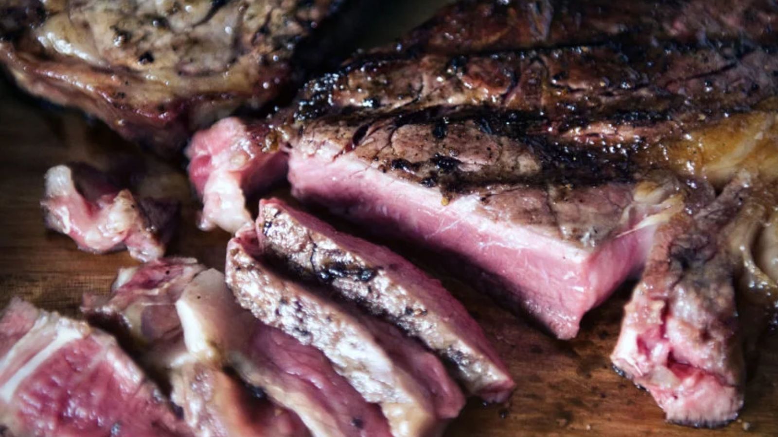 Sliced medium-rare steak on a wooden cutting board, showcasing a pink interior and brown seared exterior, perfect for surf and turf recipes for Valentine's Day.