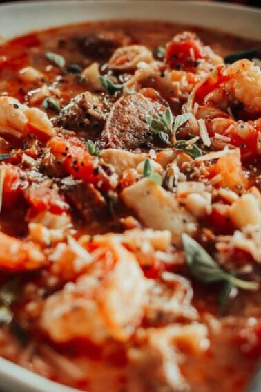 A bowl of hearty stew with vegetables, meat, and herbs, topped with grated cheese.
