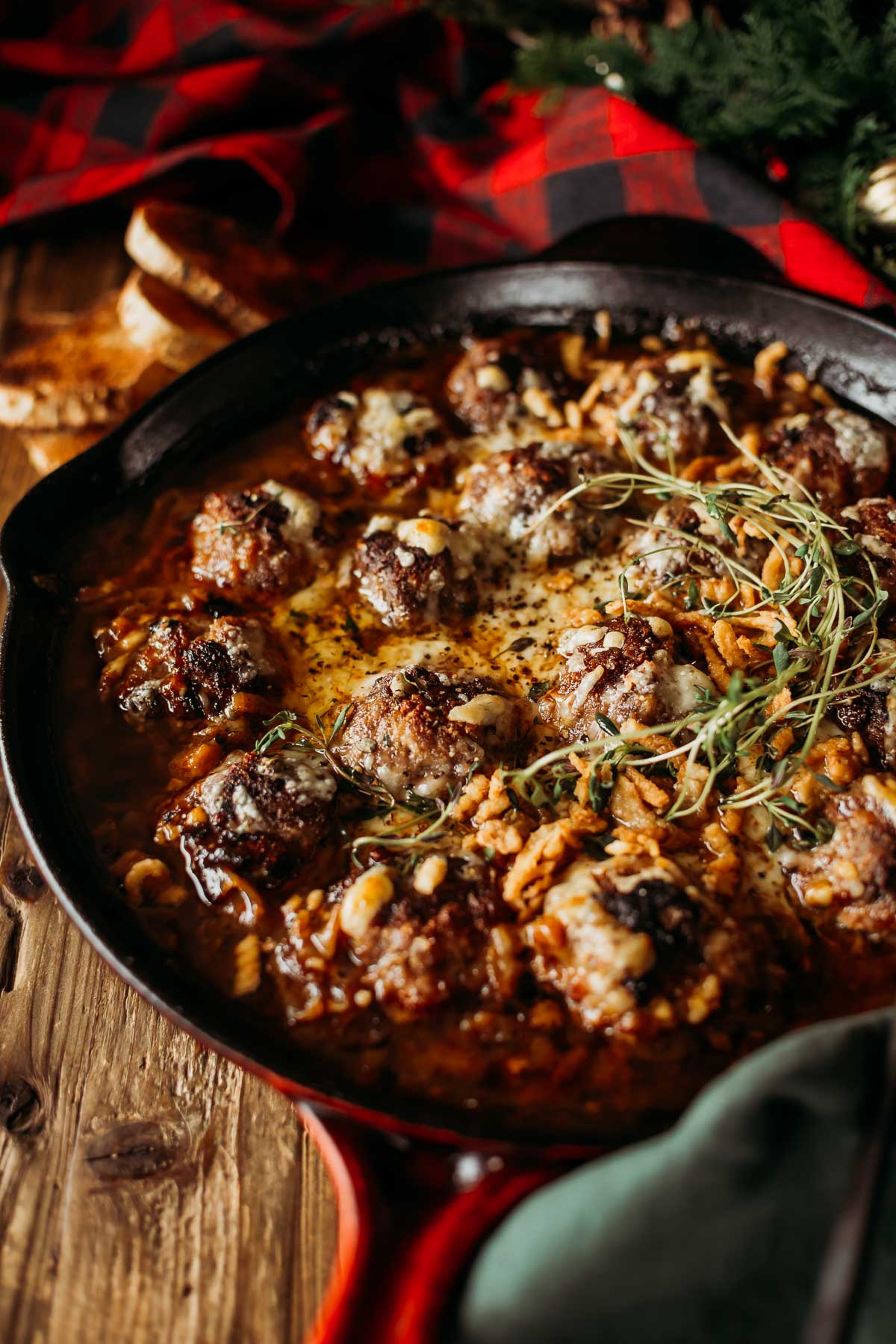 A cast iron skillet with baked french onion meatballs in sauce, garnished with herbs and crispy onions.