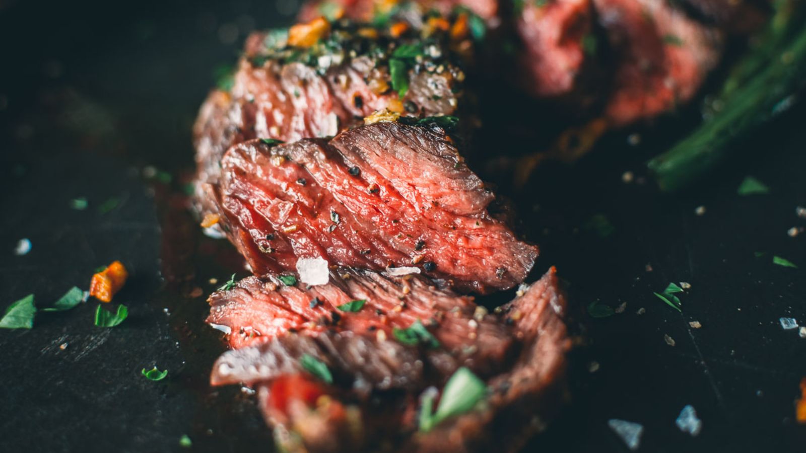 Close-up of sliced medium-rare steak, part of a delectable surf and turf recipe for Valentine's Day, garnished with chopped herbs on a dark surface.