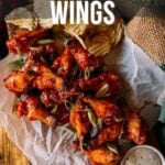 A plate of sticky honey sriracha chicken wings on parchment paper with potato chips and a side of dipping sauce.