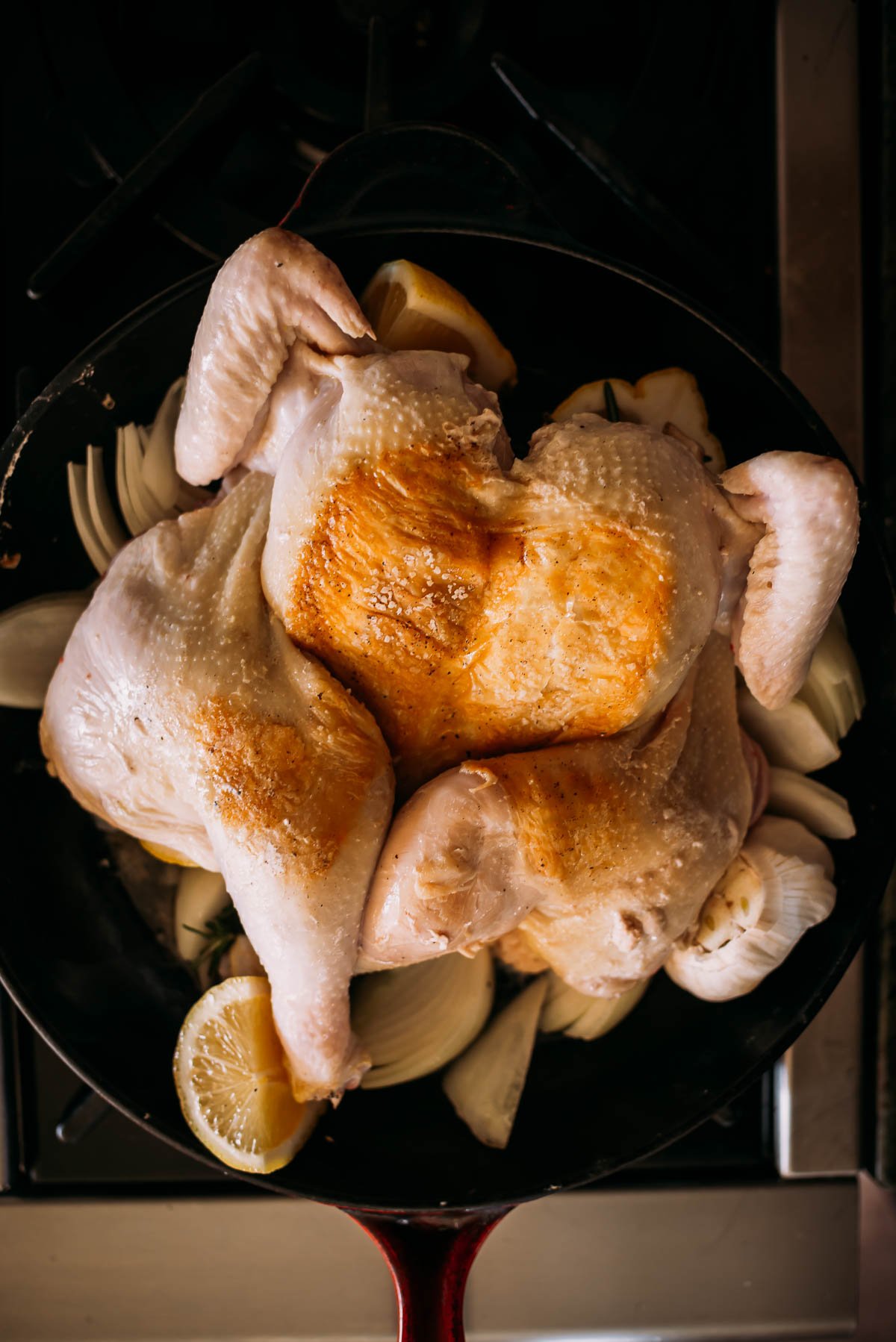 Whole raw chicken placed in a skillet with sliced onions and lemon, ready for cooking.