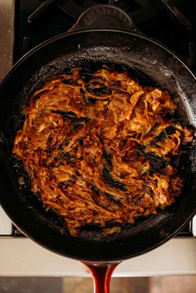 Caramelized onions in a cast iron skillet on a stovetop.