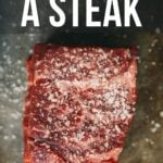 Raw steak glistening with coarse salt on a dark surface, text above perfectly captures the essence: "How to Dry Brine Steak.