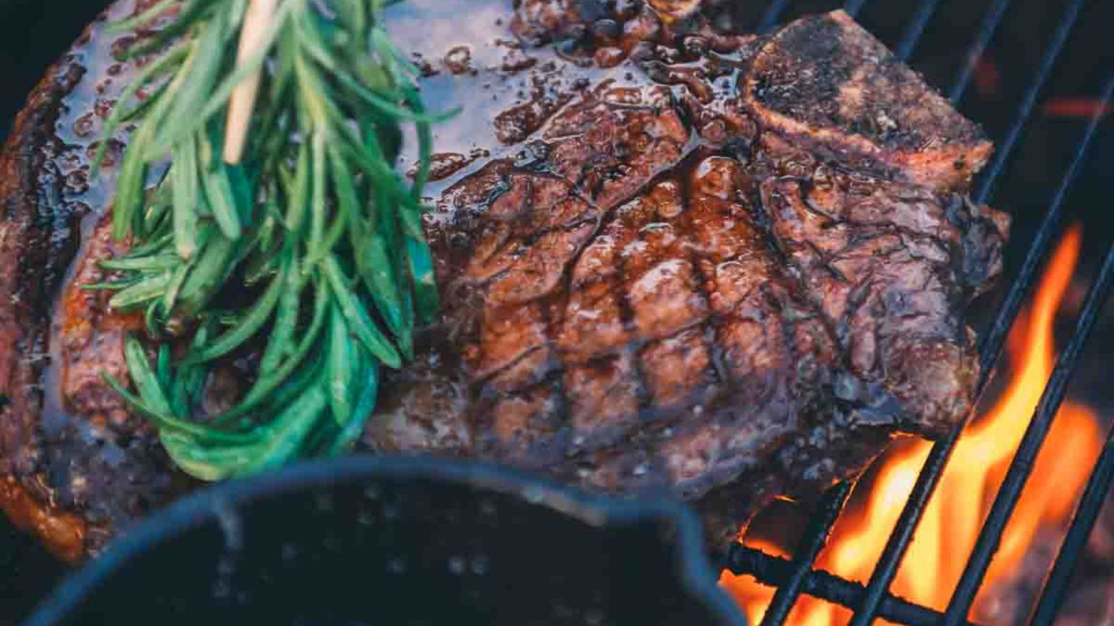 Grilled steak on a barbecue, topped with sprigs of rosemary and visible flames, makes an irresistible centerpiece for surf and turf recipes perfect for Valentine's Day.