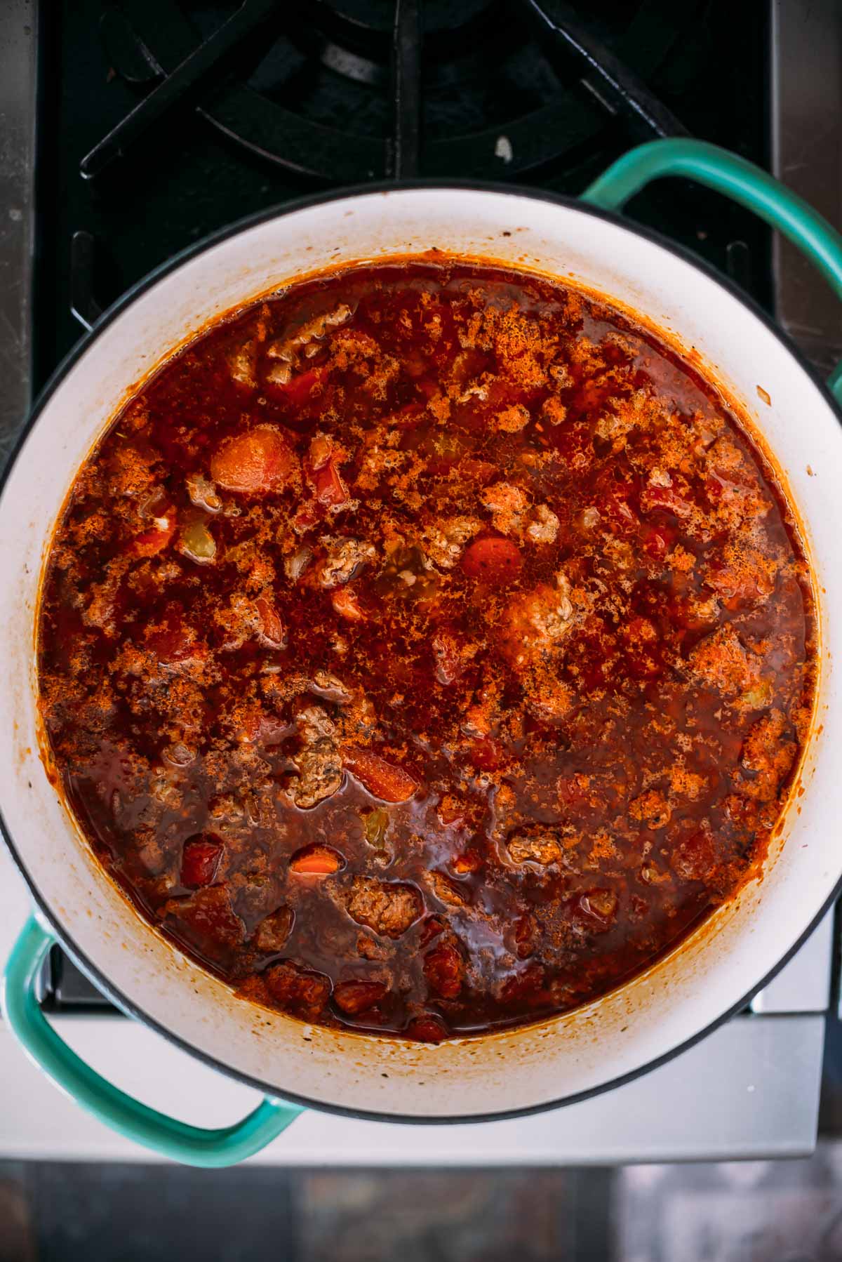 Large pot of simmering soup with visible ground sausage, carrots, and rich red broth on a stove.