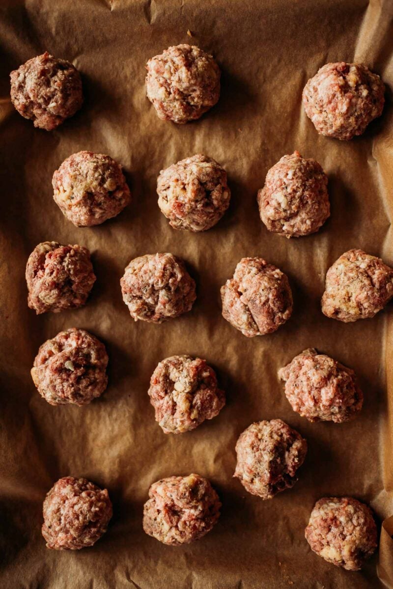 Raw meatballs arranged on a parchment-lined baking sheet.