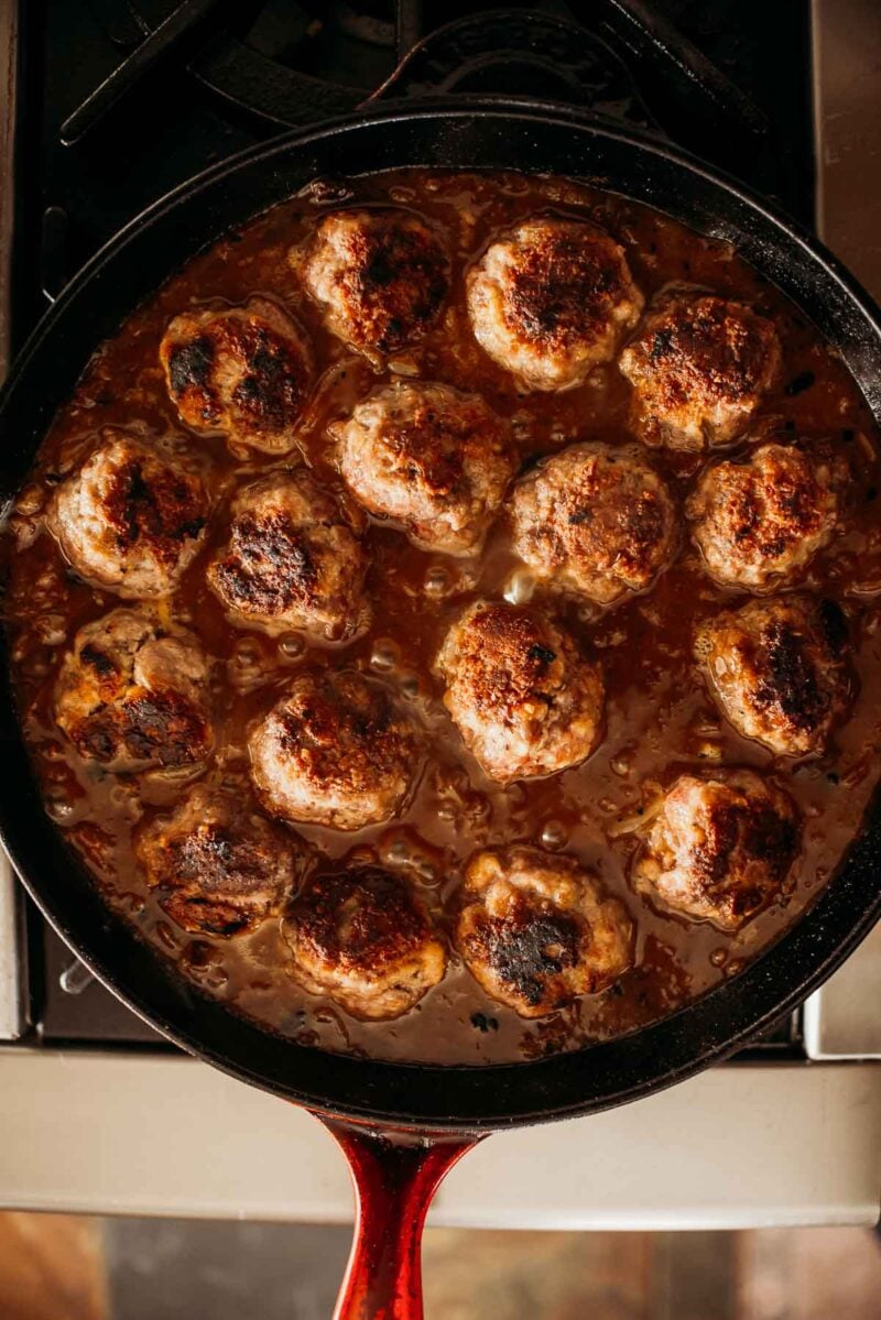 A skillet filled with evenly cooked meatballs in sauce, placed on a stove.