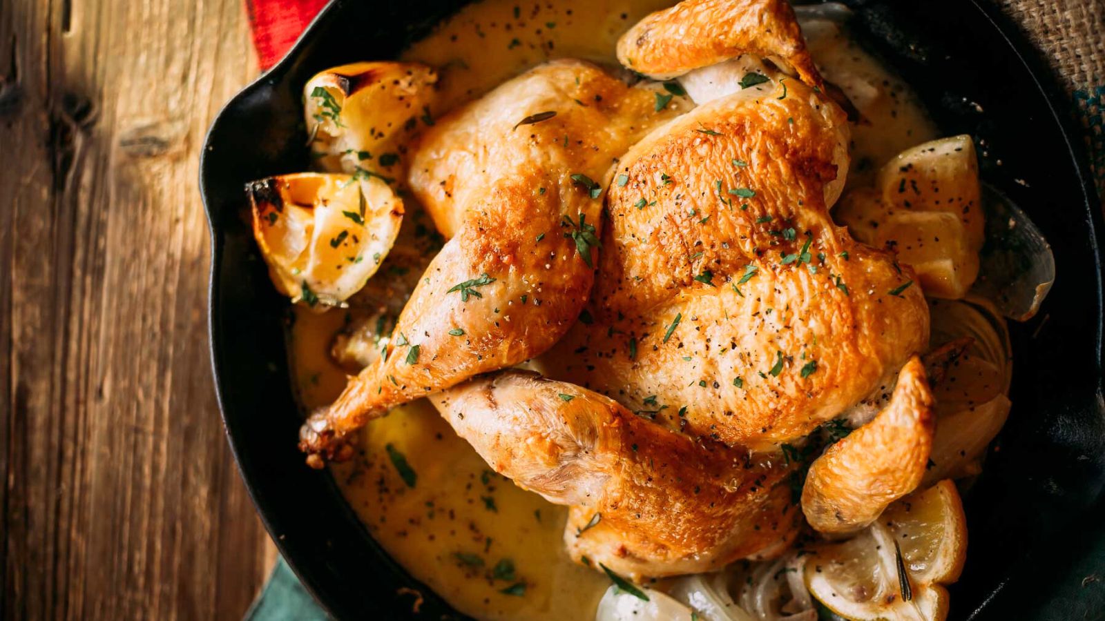 Roasted chicken with lemon wedges and herbs in a black skillet.