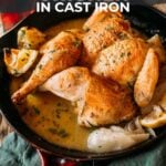 Pinterest image: Roasted lemon garlic chicken in a cast iron skillet with onions, garnished with herbs.