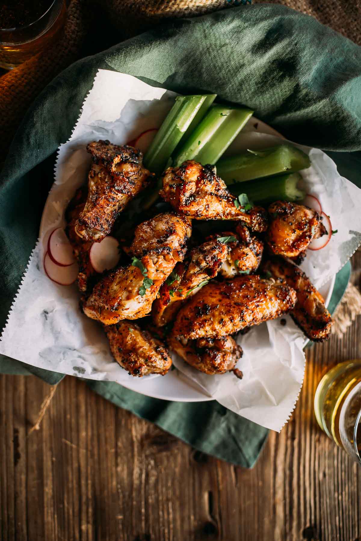 Lemon pepper chicken wings served with celery sticks on parchment paper over a green cloth on a wooden table.