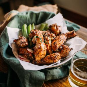 Plate of lemon pepper wings with celery sticks and beer on a wooden table.