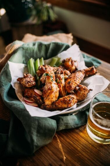 Plate of lemon pepper wings with celery sticks and beer on a wooden table.