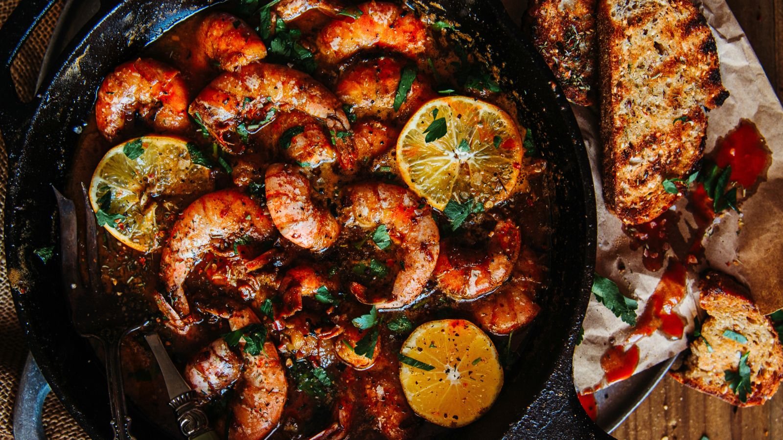 A skillet filled with cooked shrimp, garnished with lemon slices and herbs, evokes a delightful Valentine's Day vibe. This dish pairs beautifully with toasted bread drizzled in sauce, offering a tantalizing start to your surf and turf recipes collection.