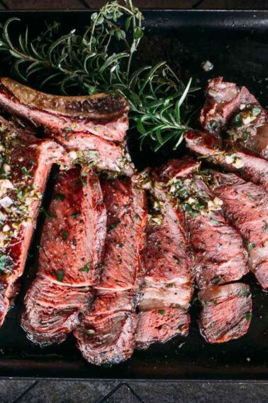 Sliced, cooked steak garnished with herbs on a black rectangular tray provides the perfect base for surf and turf recipes, ideal for an intimate Valentine's Day dinner.