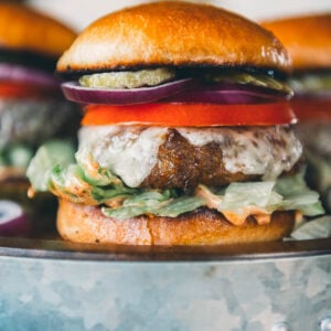 A turkey burger with lettuce, tomato, red onion, pickles, and aioli in a bun, served on a metal tray.