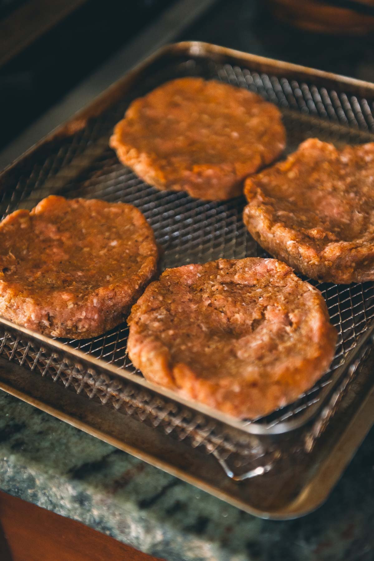Four raw turkey burger patties are placed on a wire rack over a baking tray, ready to be cooked.
