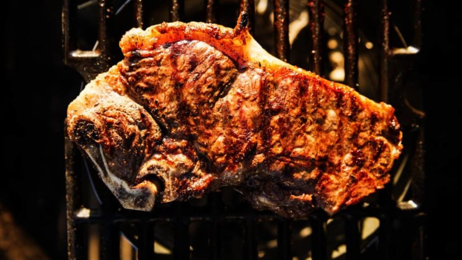 A cooked steak with grill marks sits on a barbecue grill.