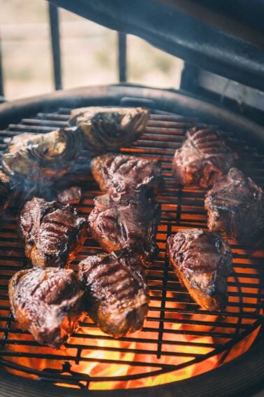 Lamb loin chops and artichoke halves are being grilled over an open flame on a barbecue grill.