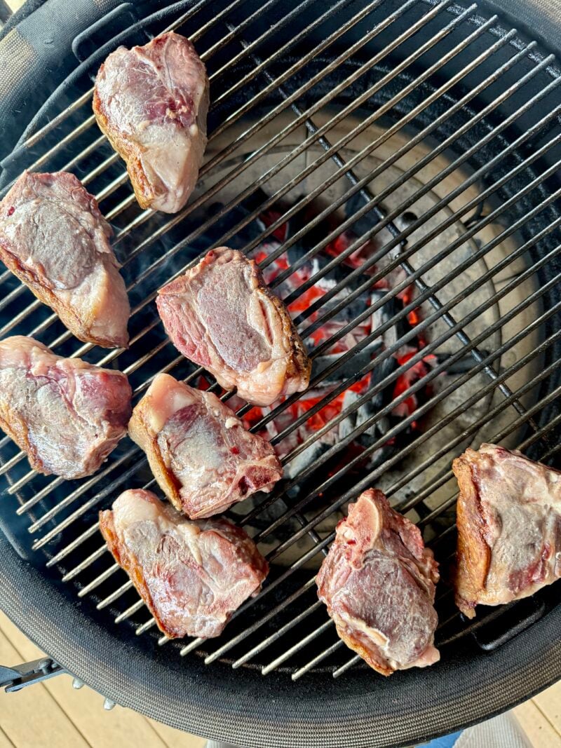 Eight pieces of raw grilled lamb loin chops are placed on a round grill over hot coals, ready to be cooked.