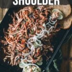 A tray of shredded smoked picnic shoulder topped with sliced onions, served with two slices of bread and a side of coleslaw.