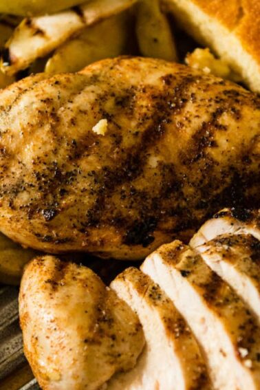 Grilled chicken breast, sliced and whole, served with cornbread and grilled vegetables on a plate.