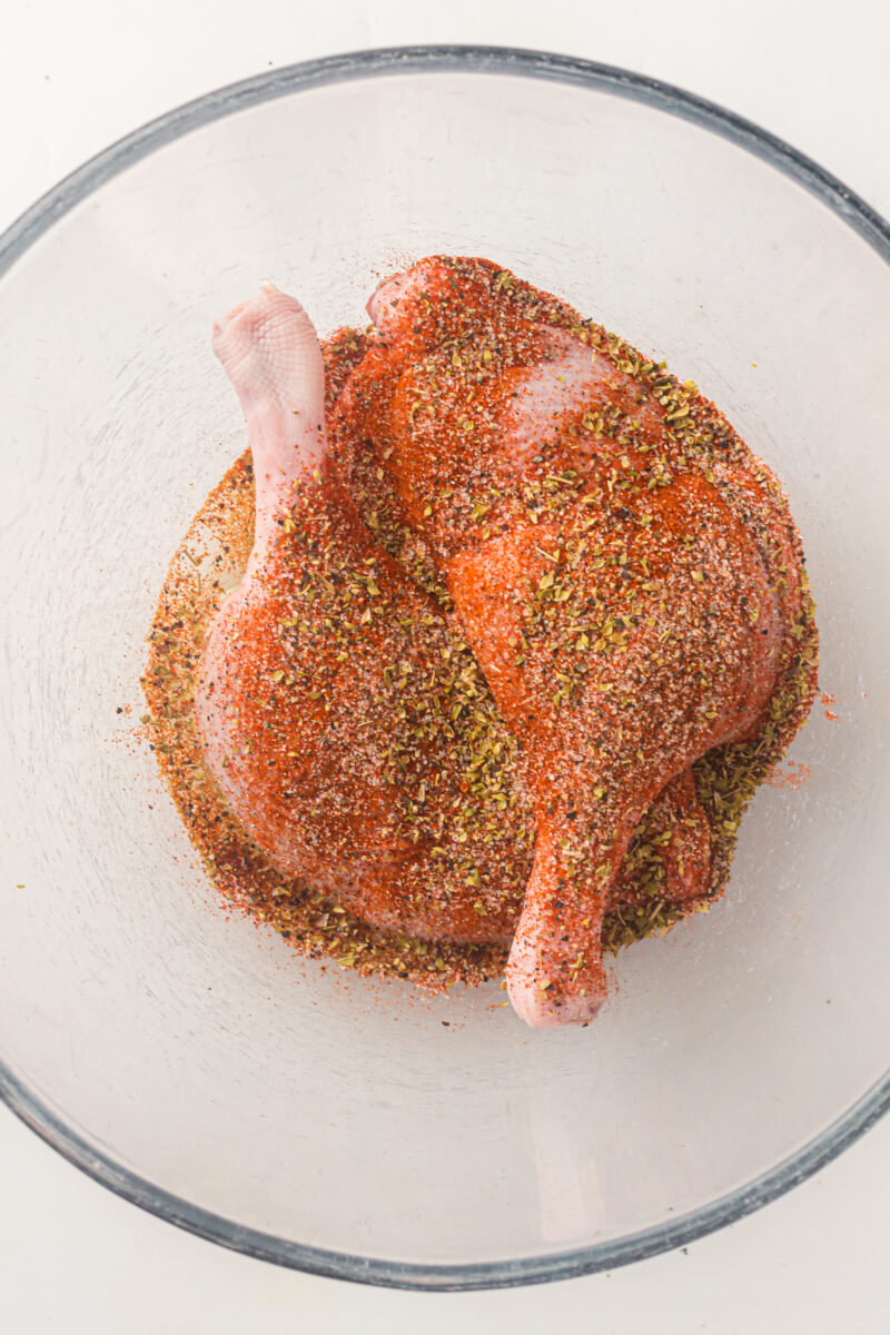 Two raw duck legs coated with a dry spice rub are placed in a clear glass bowl.