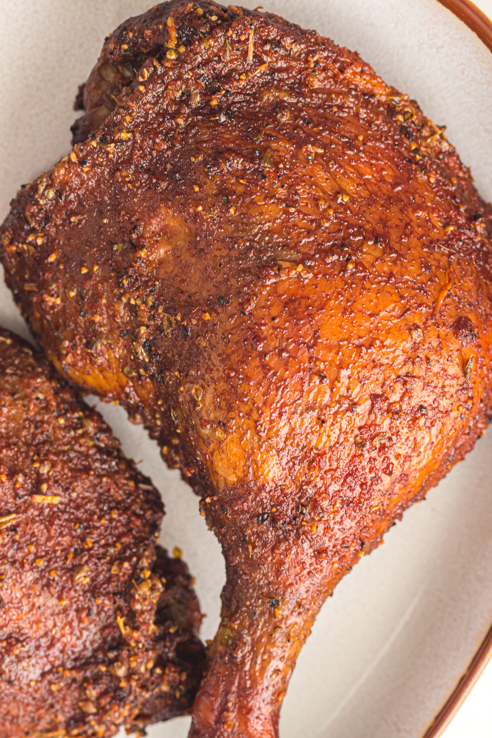 Close-up of two pieces of seasoned, smoked duck legs on a ceramic plate.
