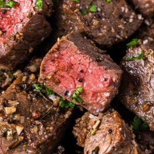 Close-up of air fryer steak bites, seasoned with herbs, garlic, and pepper, showing a pink, medium-rare center and garnished with chopped parsley.