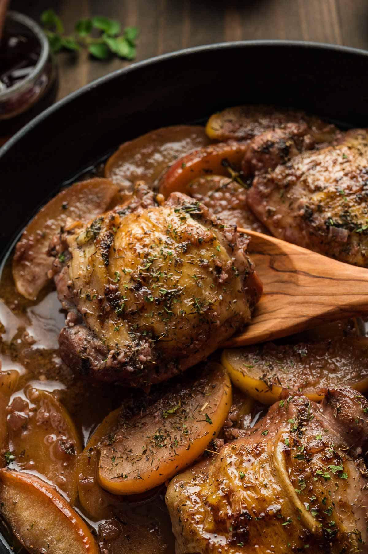 Chicken thighs and sliced apples cooked in a skillet with a brown sauce, garnished with herbs.